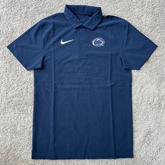 a blue nike polo shirt with the penn state logo on it, laying on a carpet