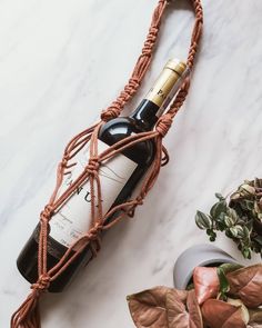 a bottle of wine tied to a rope on a marble counter top next to potted plants