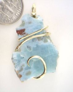 31.61ct Larimar Freeform Shard in 14kt Gold Wire Wrap Pendant 31.61 carats total weight Check Out Our Other Auctions and Ebay Store! Total weight 31.61 carats including wrap Size 37 mm by 22 mm by 7 mm including wrap     Up for sale is a beautiful rare polished Larimar piece in a hand forged 14kt gold art wire wrap. This gorgeous stone is polished to a high sheen on the front. It has a fascinating blend of bright whites and brilliant blues. To top it all off are the swirling waves of glowing 14kt gold securely gripping the stone and really making it pop. Truly a perfect piece and it could be yours!!   Larimar is a new and rare gemstone that has been found in only one location: in a mountainous, relatively inaccessible region of the Dominican Republic overlooking the Caribbean Sea. This gem Sea Glass Wire Wrapping, Artisan Jewelry Necklaces, Art Wire, Wire Wrap Pendant, Stone Wrapping, Handcrafted Artisan Jewelry, Rare Gemstones, Caribbean Sea, Petrified Wood