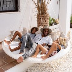 a man and two children sitting on a white hammock swing with palm trees in the background