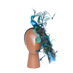 ON VACATION: Fab Hatters will be on vacation from December 20-31.  No orders will go out during this time.  If you have any questions or concerns about possible deadlines & our availability for when we return, please email us at INFO@FABHATTERS.COM Shake your tail feather in this FLOCKing fabulous peacock headband that converts into different looks!  A  blue glittered peacock is accented with a dramatic feathered tail featuring peacock eye feathers and various other feathers in shades of blue an Peacock Headband, Green Peacock, Fascinator Hat, Animal Hats, Tail Feathers, Peacock Green, Fascinator Hats, Black Satin, Fascinator