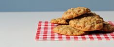 three oatmeal cookies sitting on top of a red and white checkered napkin