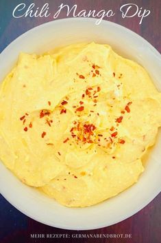 a white bowl filled with yellow food on top of a wooden table next to a knife and fork