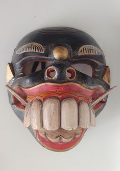 a wooden mask with teeth and fangs on it's face is hanging from the wall