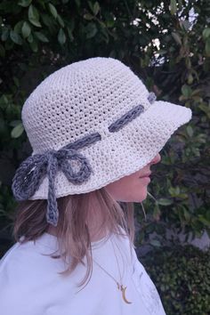 a woman wearing a white crocheted hat with grey ribbon on the brim