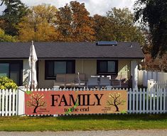 a sign that says family to the end in front of a white picket fence and house