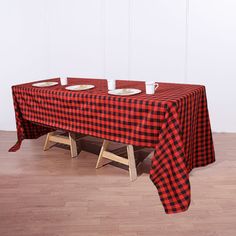 a red and black checkered table cloth with place settings on it, sitting in front of a white wall