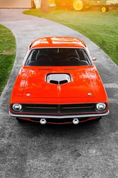 an orange muscle car parked on top of a cement road next to a grass covered field