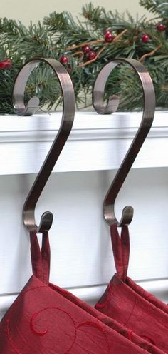 two red towels hanging from hooks on a window sill with evergreen branches in the background