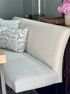 a couch with pillows on it next to a wooden table and flowers in vases