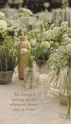 a table topped with vases filled with flowers and greenery next to a candle