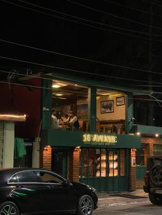 a black car parked in front of a green building at night with the lights on