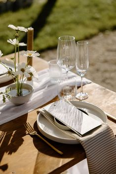 the table is set with white plates, silverware and flowers in glass vases