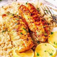 two pieces of fish on a plate with rice and lemons next to a fork