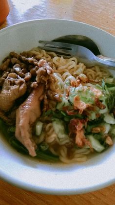 a white bowl filled with noodles and meat on top of a wooden table next to an orange drink