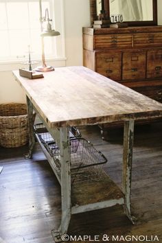 an old wooden table with baskets on it in front of a mirror and dresser next to a window