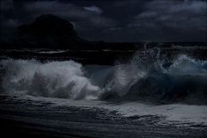 an ocean wave crashing into the shore at night