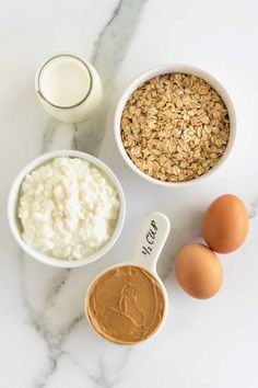 ingredients for peanut butter oatmeal in bowls on a marble countertop next to an egg, milk, and yogurt