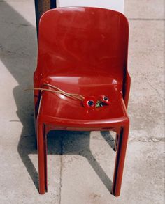 a red chair sitting on the sidewalk next to a pole with two buttons attached to it