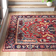 a red and blue rug on the floor next to some stairs with a plant in it