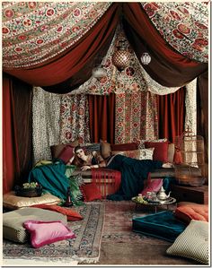 a woman laying on top of a bed covered in red and brown curtains next to a bird cage