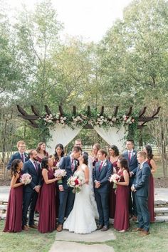 a bride and groom with their bridal party in front of an outdoor ceremony arch