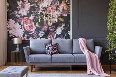 a living room with grey couches and pink flowers on the wall behind it,