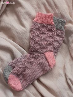 a pair of knitted socks laying on top of a white bed sheet with pink and grey colors