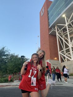 two girls in red shirts standing next to each other near a building with people walking around