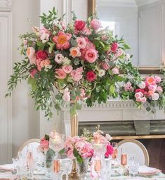 a tall vase filled with lots of pink flowers on top of a table next to a mirror