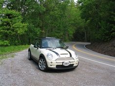 a small white car parked on the side of a road next to trees and bushes