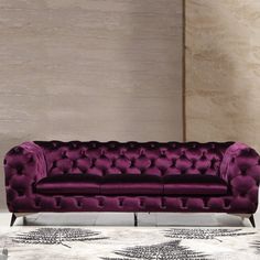 a purple couch sitting on top of a white floor next to a rug and wall