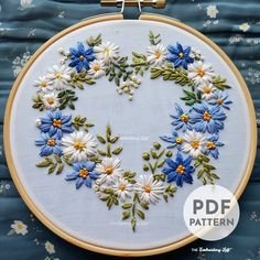 a blue and white embroidered heart with daisies in the center on a blue background