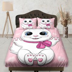 a white cat with blue eyes and pink bow on it's head sitting on a bed