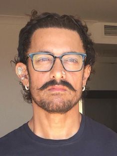 a close up of a person wearing glasses and a mustache with piercings on his ears