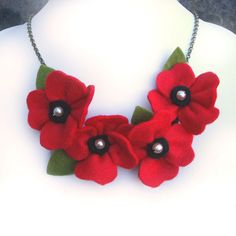 a necklace with red flowers and green leaves on a white mannequin neckline