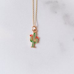 a gold necklace with a green and red cactus charm