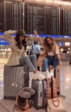 two women sitting on suitcases at an airport posing with their arms in the air