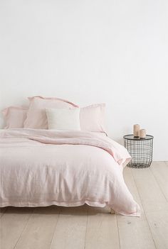 a bed with pink linens and pillows in a white room next to a wire basket