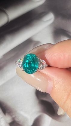 a woman's hand holding a ring with an emerald and diamond center stone on it