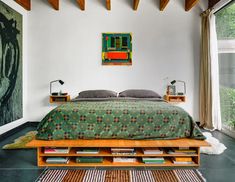 a bed sitting in a bedroom next to a window with lots of books on it