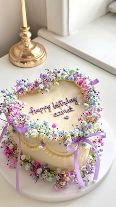 a heart shaped cake decorated with flowers on a white plate next to a gold candle