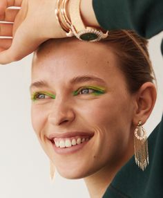 a woman with green eyeshadow and gold bracelets on her head smiling at the camera