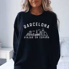 a woman standing in front of a bed wearing a black sweatshirt with barcelona written on it