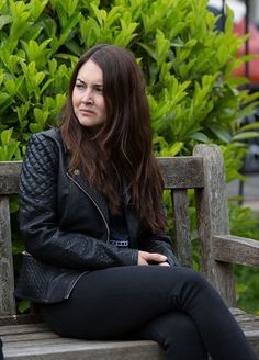 a woman sitting on top of a wooden bench next to a man in black jacket