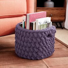 a purple knitted basket is sitting on the floor next to a couch with books in it