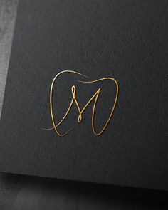 the letter m is made out of gold wire and sits on a black card board