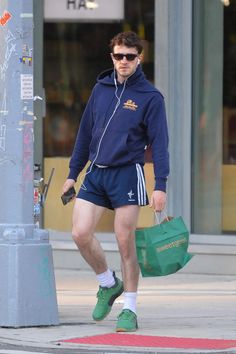 a man walking down the street with headphones on, carrying a green shopping bag