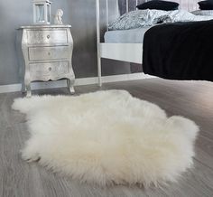 a white sheepskin rug is on the floor in front of a bed and dresser