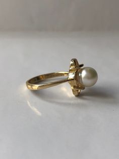 June Pearl is a vintage ring. Crafted in the mid-century in 14K yellow gold. The pearl is a natural, lustrous 6.8 millimeter round pearl. This simple ring will make a wonderful staple jewelry piece for someone who appreciates pearls or has a June birthday or anniversary month. The ring is very comfortable on the hand and tapers from 1mm to 2.18mm at the bottom of the shank. Currently a size 5.5 (Can be sized up or down upon request) Every Antique piece of jewelry we sell at Heirloom Pavé has bee Vintage Pearl Ring With Gemstone, Classic Gemstone Flower Ring For Wedding, Classic Wedding Flower Ring With Gemstone, Vintage Gold Hallmarked Pearl Ring, Vintage Yellow Gold Pearl Ring With Gemstone, Vintage Oval Pearl Ring For Gift, Vintage Oval Pearl Ring Gift, Adjustable Oval Pearl Ring For Wedding, Antique Gold Pearl Ring For Wedding